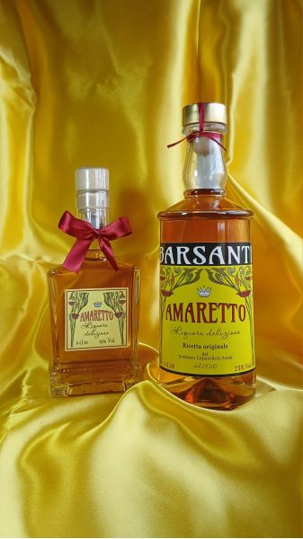 Due bottiglie di Amaretto Barsanti, decorate con fiocchi rossi, esposte su un drappo di raso giallo dorato.