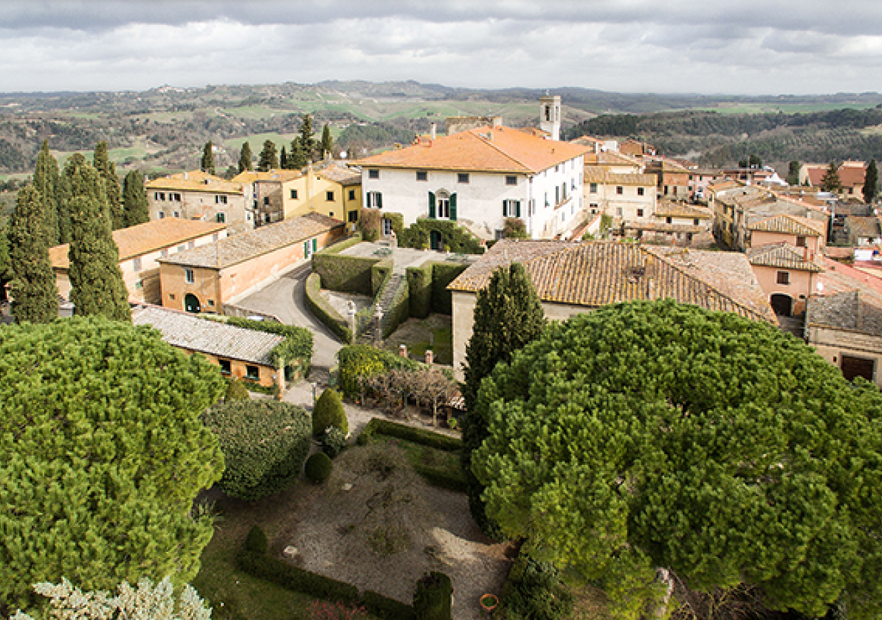 Veduta dall’alto della Tenuta di Ghizzano e del borgo circostante, con la villa, il giardino all’italiana, i tetti in cotto e le colline delle Terre di Pisa sullo sfondo.