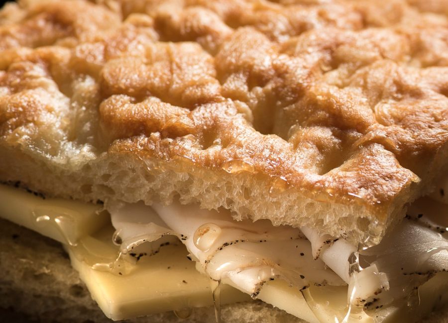 Focaccia dorata e croccante farcita con formaggio e sottili fette di lardo, completata da miele che cola dalla farcitura.