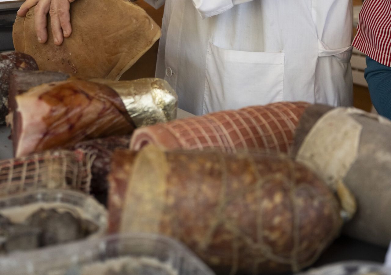 Banco di macelleria con salumi e insaccati artigianali, mentre due addetti in camice bianco servono i prodotti.