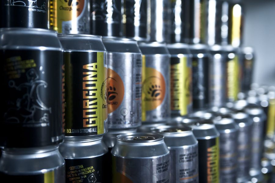 Lattine di birra artigianale OrzoBruno disposte in file, con diverse etichette e referenze del birrificio in primo piano e sullo sfondo.