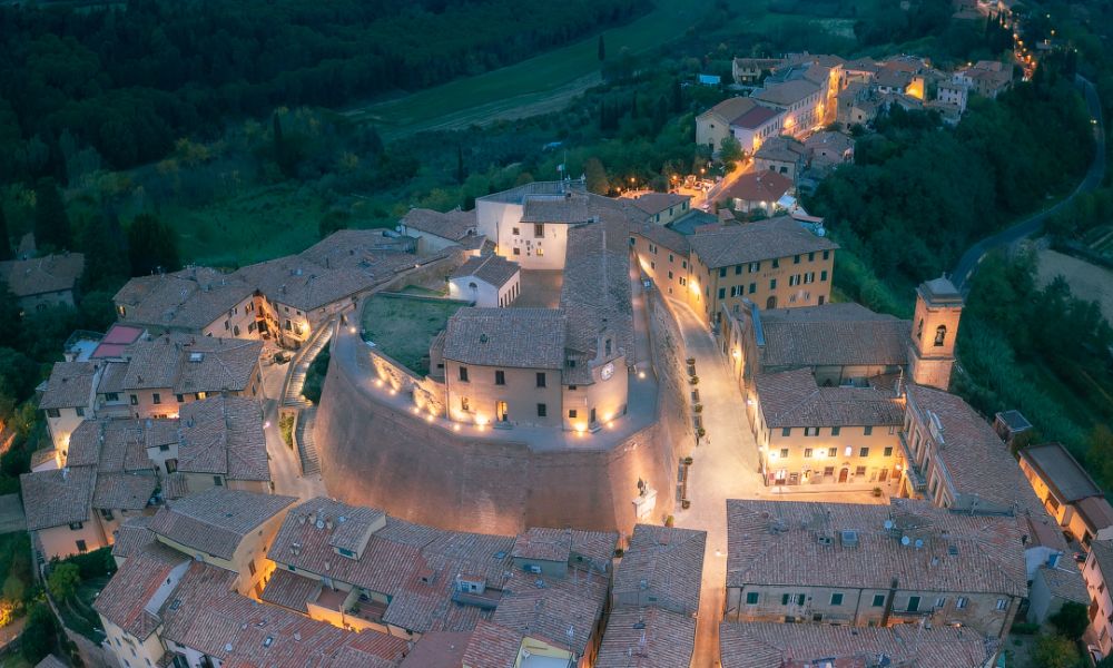 Veduta aerea del borgo di Peccioli, nelle Terre di Pisa, con tetti in laterizio, campanile storico, terrazza panoramica e paesaggio collinare sullo sfondo.