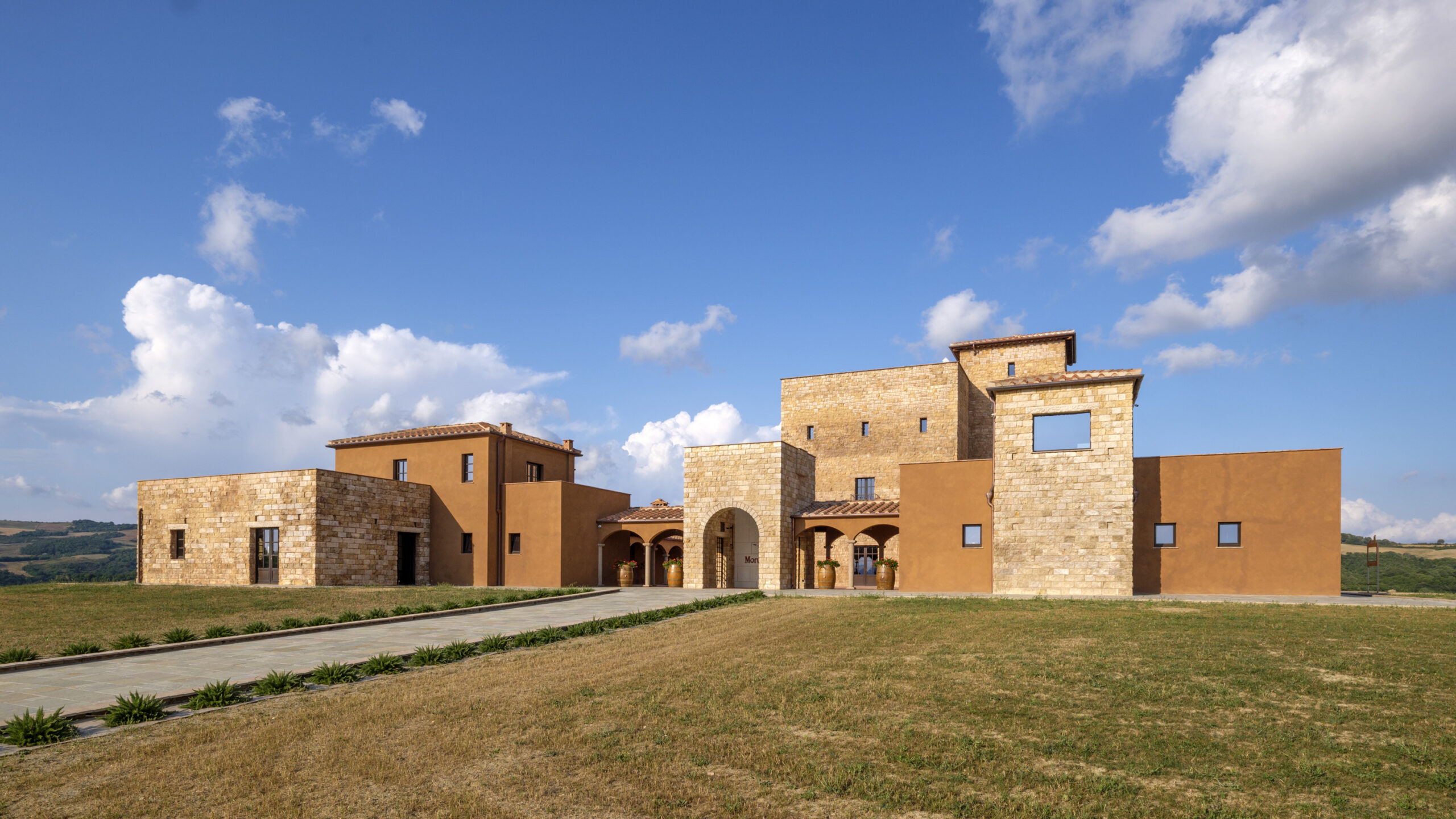 Edificio della cantina MonteRosola, realizzato in pietra e intonaco color terra, immerso nelle colline di Volterra sotto un ampio cielo azzurro.