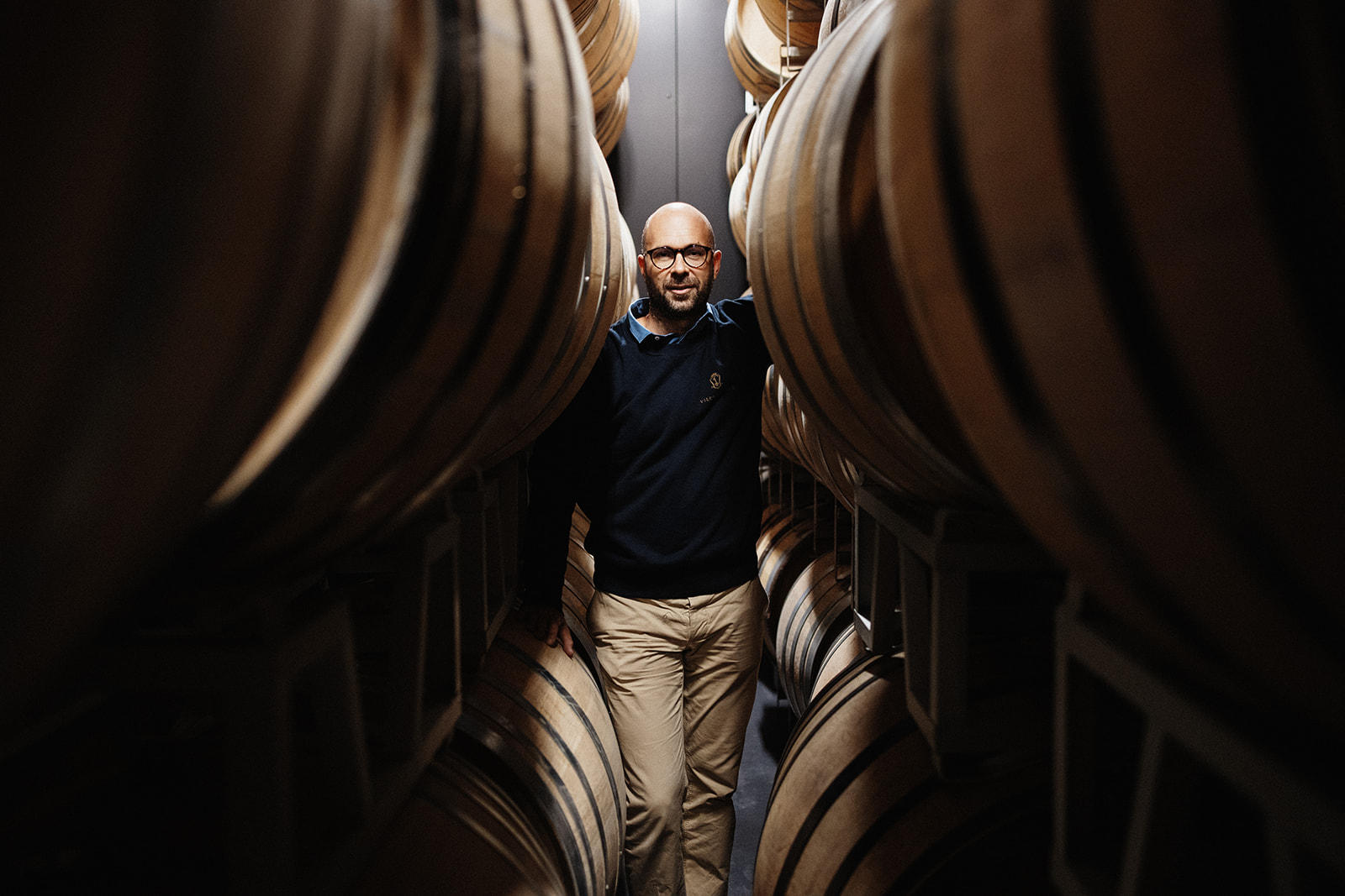 Uomo in piedi tra grandi botti di legno all’interno della cantina di Villa Saletta.