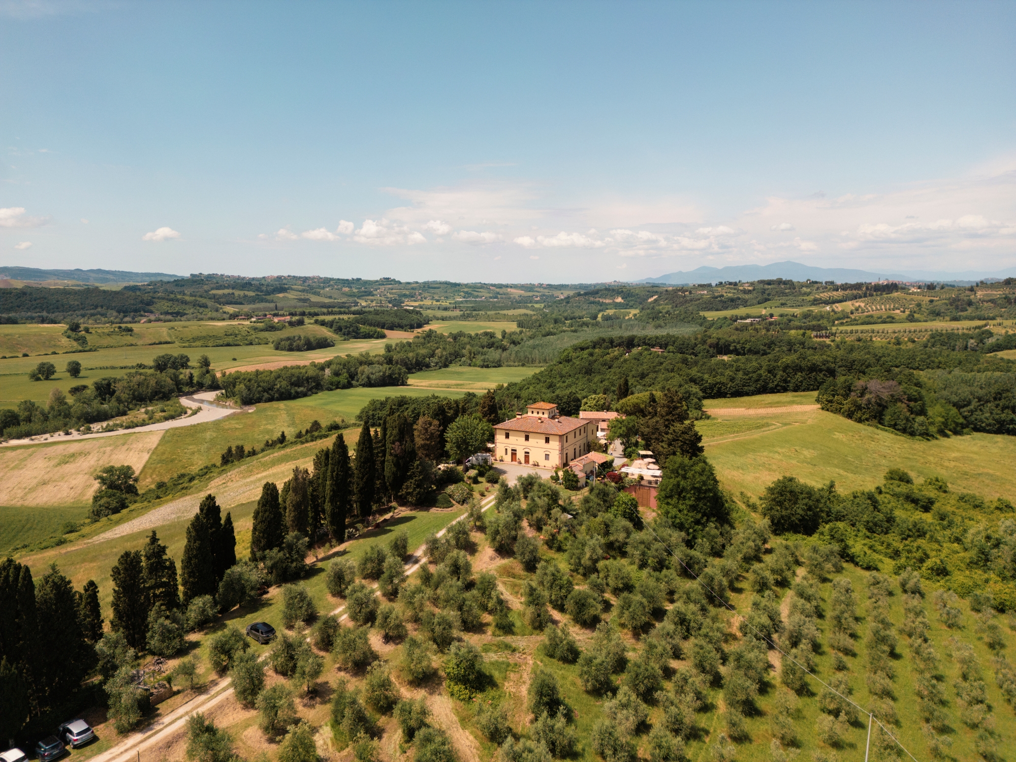 Veduta aerea dell’Azienda Agricola I Moricci, con la villa circondata da oliveti, cipressi e verdi colline nel paesaggio rurale di Peccioli.