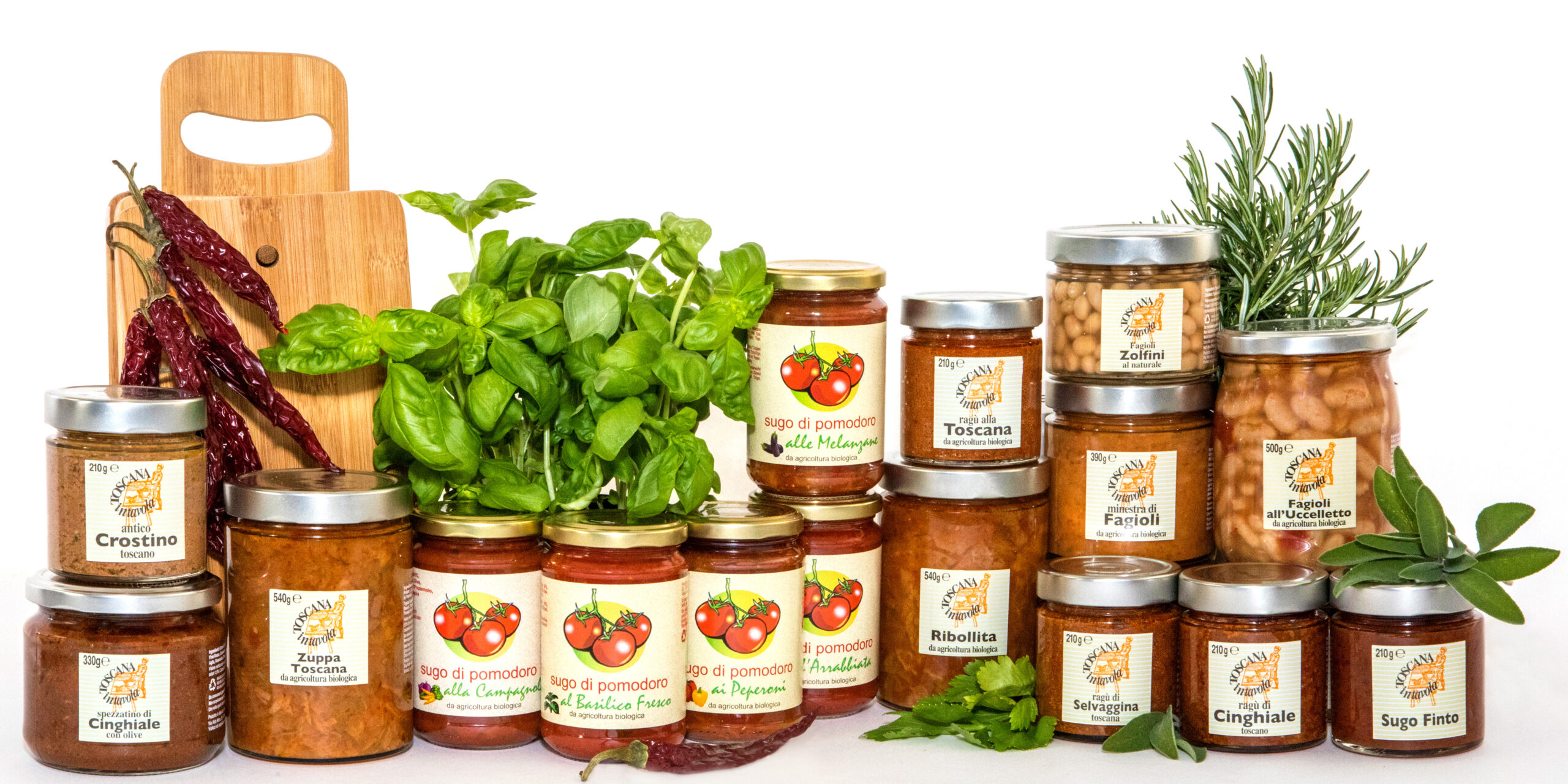Assortimento di conserve e specialità toscane in barattolo di vetro, tra cui sughi di pomodoro, ragù, zuppe, legumi e salse per crostini, disposti con basilico, rosmarino, salvia e peperoncini secchi.