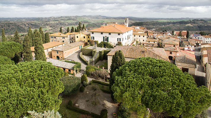 Veduta dall’alto della Tenuta di Ghizzano e del borgo circostante, con la villa, il giardino all’italiana, i tetti in cotto e le colline delle Terre di Pisa sullo sfondo.