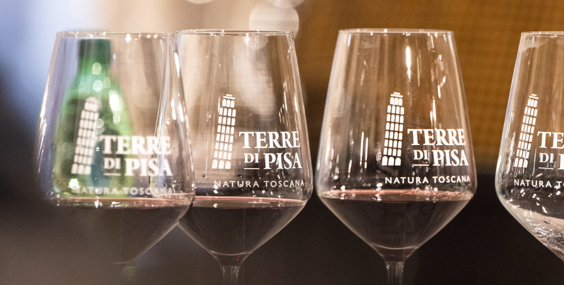 Calici da degustazione con il logo Terre di Pisa, alcuni contenenti vino rosso, disposti in primo piano durante una masterclass enologica.