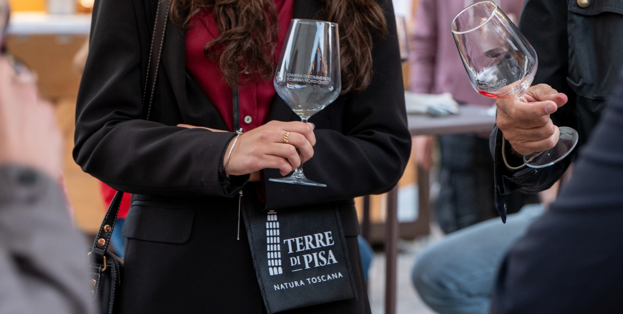 Partecipanti a un tour di degustazione tengono in mano calici da vino e una shopper Terre di Pisa durante il Festival.