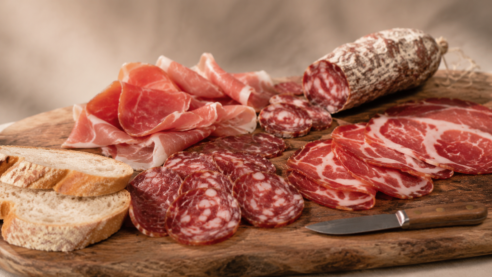 Tagliere di salumi di Cinta senese con prosciutto, capocollo e salame affettati, accompagnati da pane su uno sfondo neutro e sfocato.