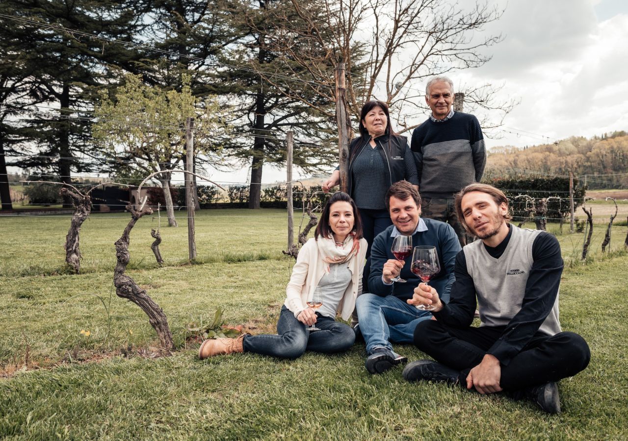 Famiglia di Podere Pellicciano ritratta tra i filari della tenuta sulle colline di San Miniato; alcune persone tengono in mano calici di vino rosso.
