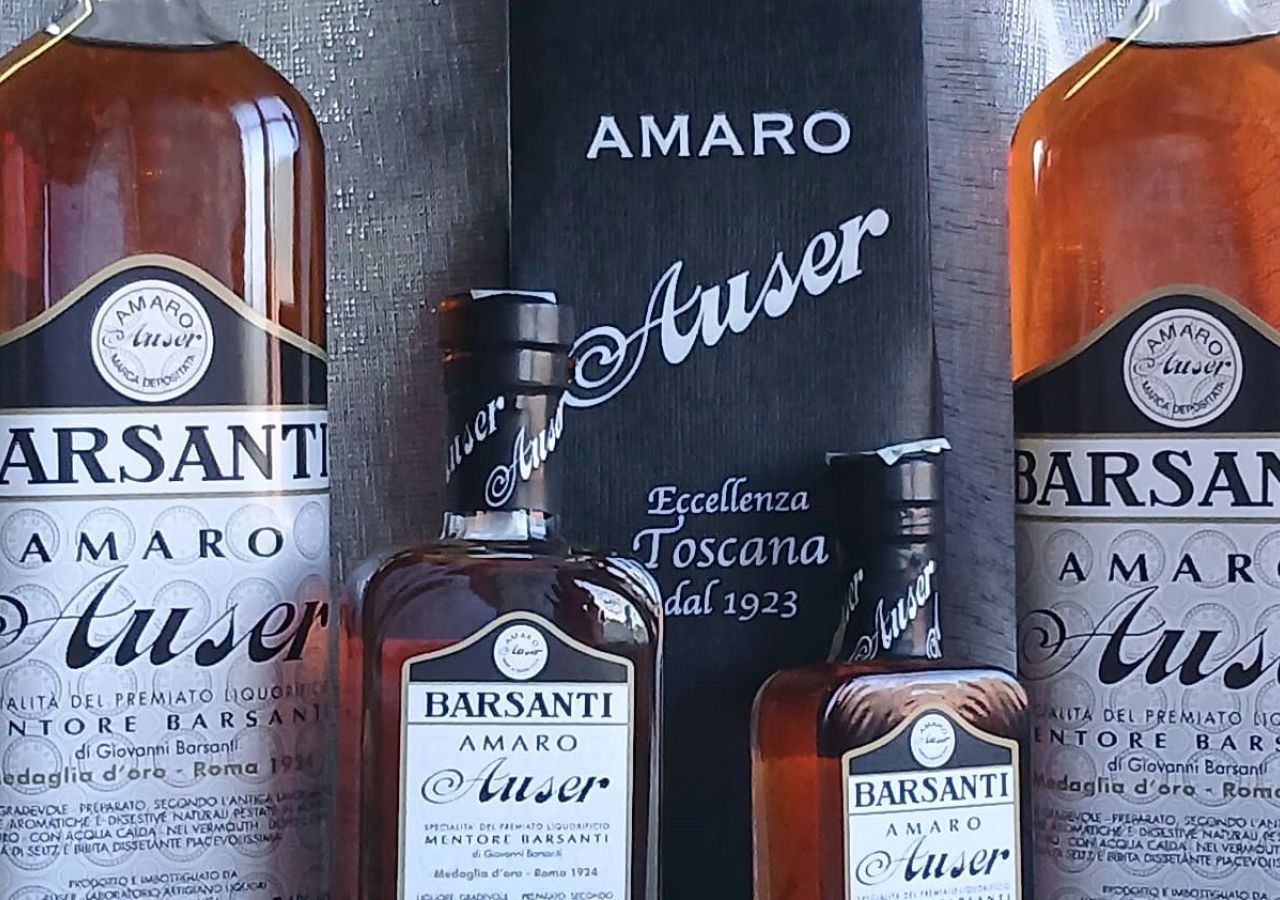Quattro bottiglie di Amaro Auser Barsanti in diversi formati, affiancate da una confezione nera con la scritta “Eccellenza Toscana dal 1923”.