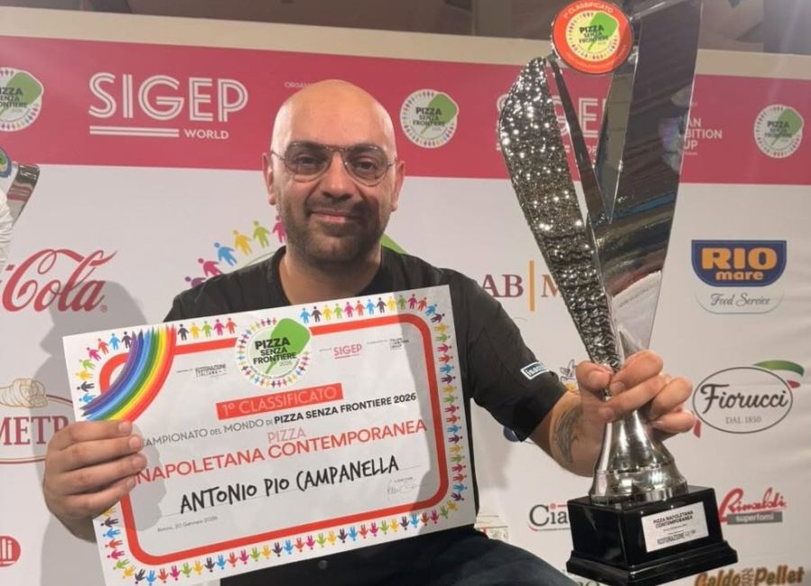 Pizzaiolo sorridente con in mano il certificato di primo classificato nella categoria pizza napoletana contemporanea e un grande trofeo, durante il Campionato del Mondo di Pizza Senza Frontiere 2026 al SIGEP.