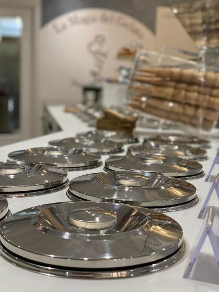 Interno de La Magia del Gelato, con coperchi in acciaio lucido sul banco gelateria e contenitori di cialde sullo sfondo.