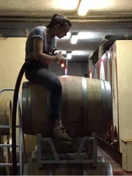 Operatrice seduta su una botte all’interno della cantina, mentre controlla le attrezzature durante una fase di lavorazione del vino.