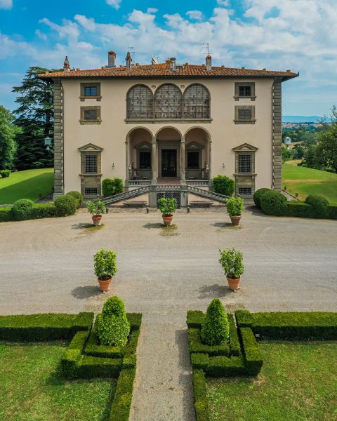 Vigneti sulle colline toscane illuminati dalla luce del tramonto, con filari di cipressi, un casale e il profilo delle montagne sullo sfondo.