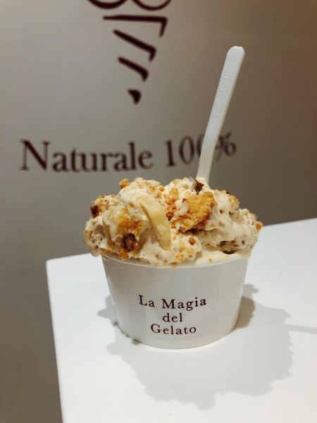 Biscotto gelato artigianale farcito con crema chiara, servito in un tovagliolino e tenuto in mano, con sfondo sfocato del banco gelateria.