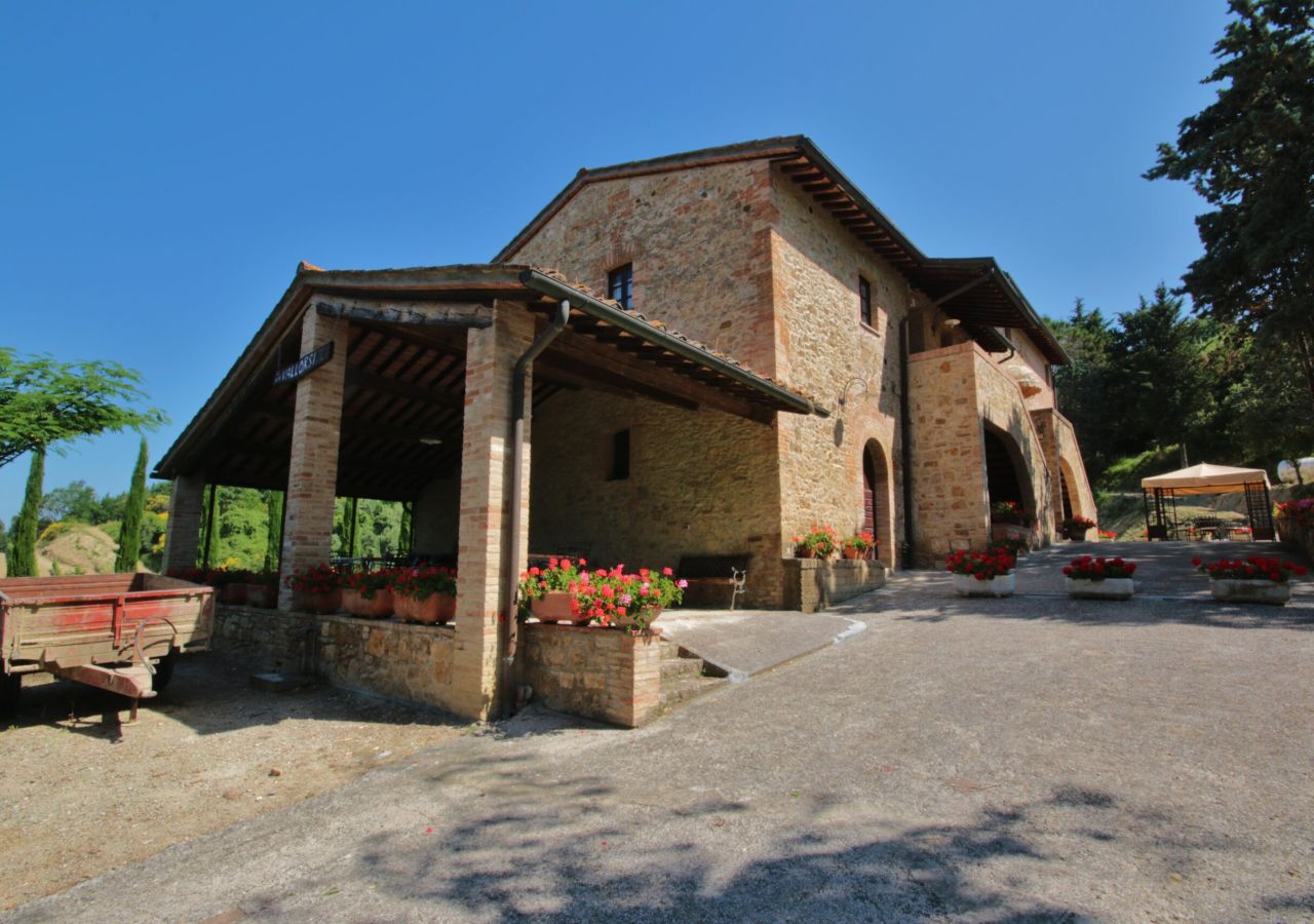 Edificio rurale in pietra dell’Azienda Agricola Vallorsi, con porticato, vasi di fiori rossi e spazi esterni immersi nel verde delle colline pisane.