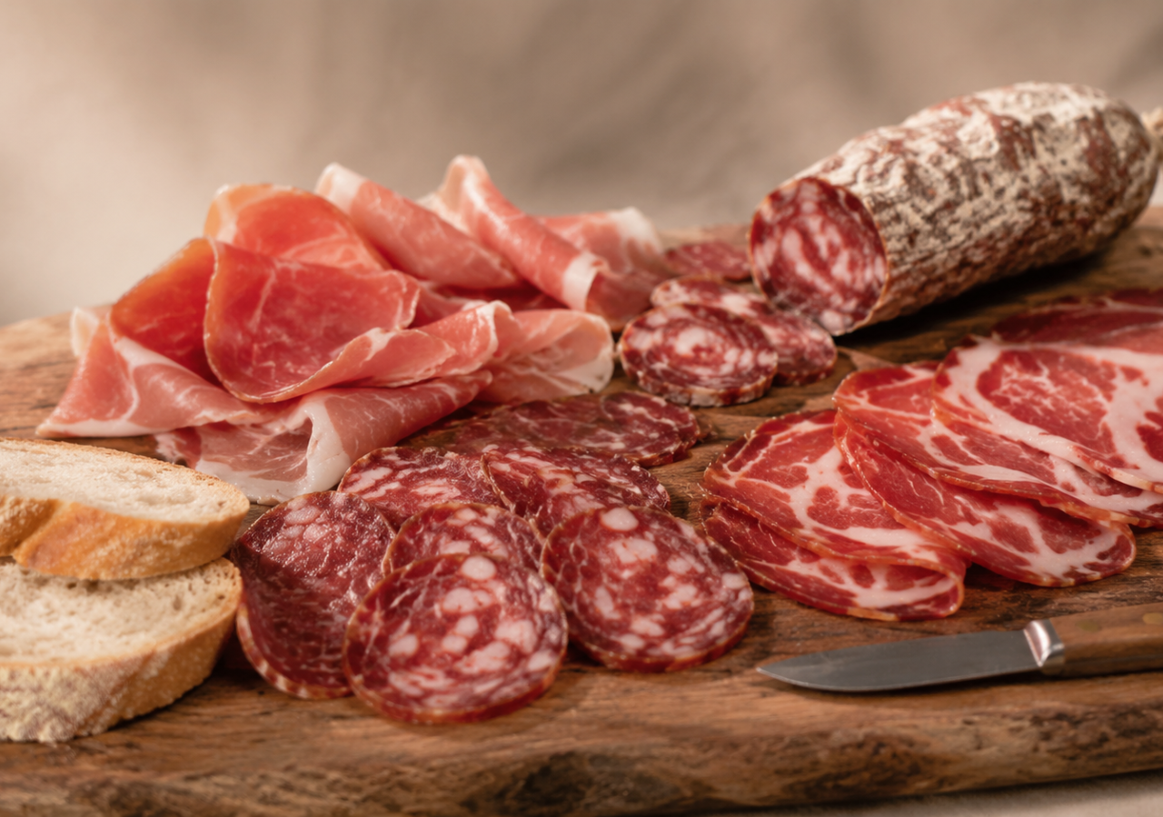Tagliere di salumi di Cinta senese con prosciutto, capocollo e salame affettati, accompagnati da pane su uno sfondo neutro e sfocato.