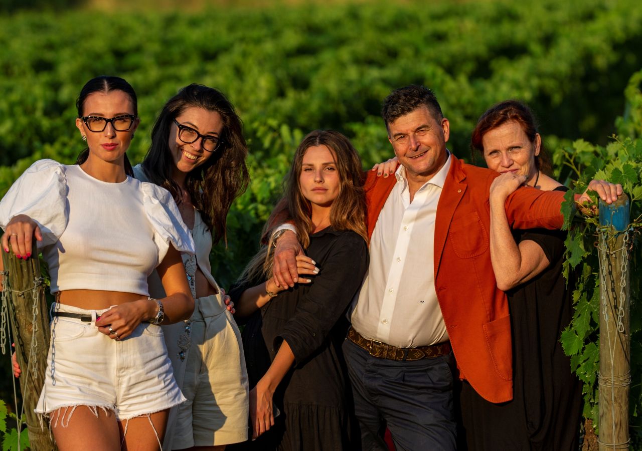 La famiglia dell’azienda vinicola L’Agona posa tra i filari della tenuta di Terricciola, illuminata dalla luce calda del tramonto.