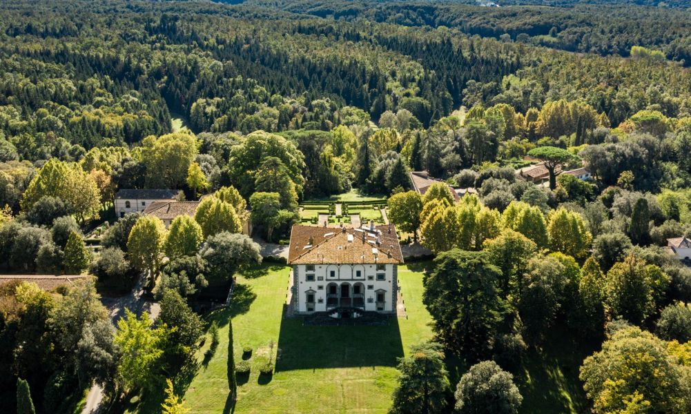 Veduta aerea di Villa Varramista, circondata dal parco, dal giardino all’italiana e dagli edifici storici della tenuta, immersi in un vasto paesaggio boschivo.