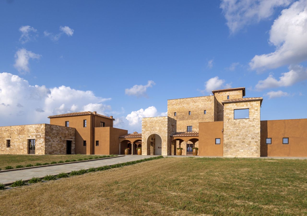 Edificio della cantina MonteRosola, realizzato in pietra e intonaco color terra, immerso nelle colline di Volterra sotto un ampio cielo azzurro.