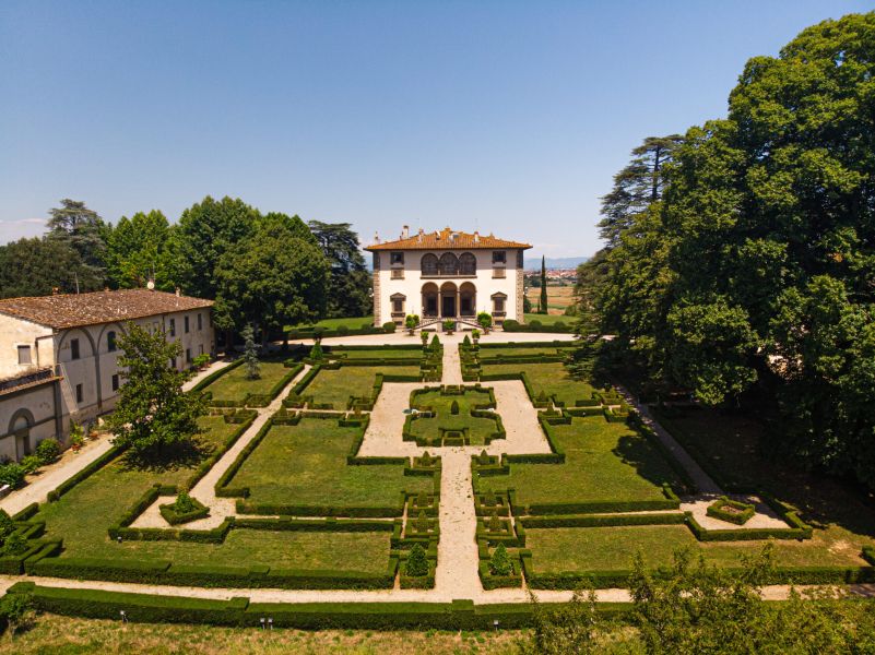 Veduta aerea del giardino all’italiana di Villa Varramista, con siepi geometriche, vialetti in ghiaia e la villa sullo sfondo, circondata da grandi alberi.